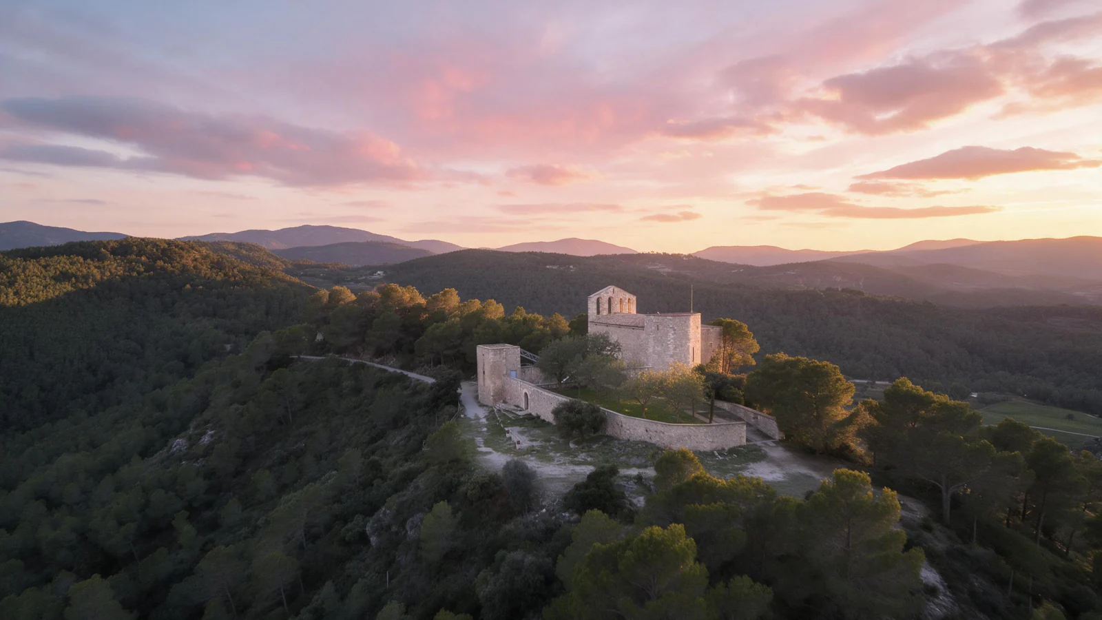 El santuari de Santa Maria de Foix i el seu recinte emmurallat al capvespre, dalt del turó entre pinedes, amb les serres del Penedès al fons i el cel rosat de la posta