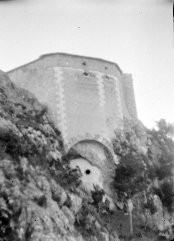 The sanctuary's apse rising above a crag, and at the foot of the rock the stone arch closing the cave entrance