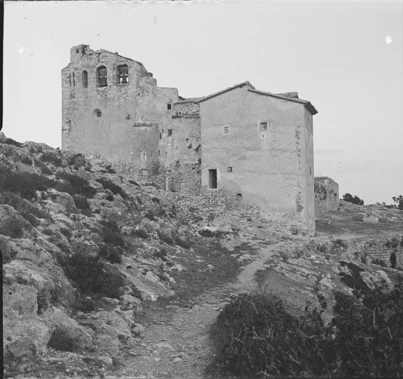 The sanctuary seen from the path up, with the bell gable and its two bells on the left, the farmhouse on the right and the rocky slope in front