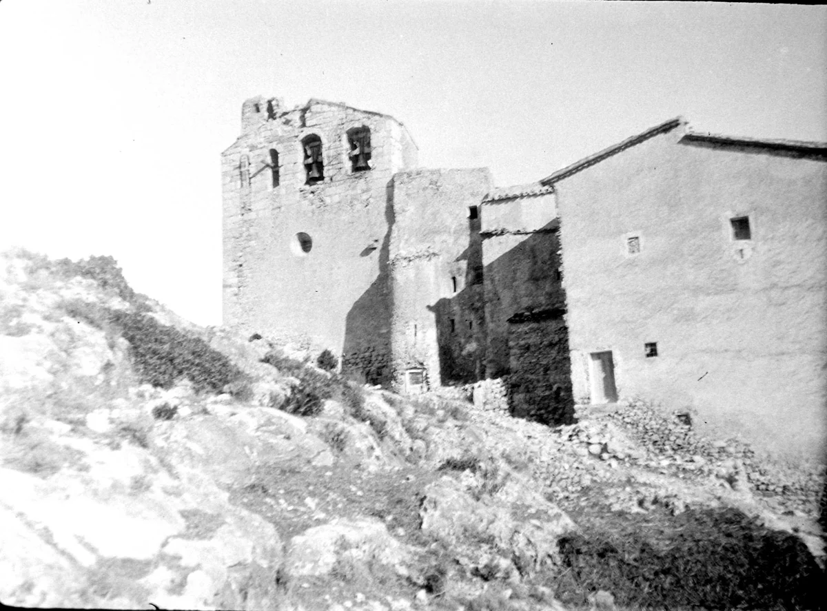 El santuario desde abajo, con el campanario de espadaña de dos ojos y las dos campanas colgadas, y el cuerpo de la masovería con el tejado entero